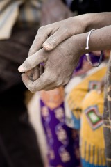 A Kokomba man clasps his hands in prayer at an outdoor church service.